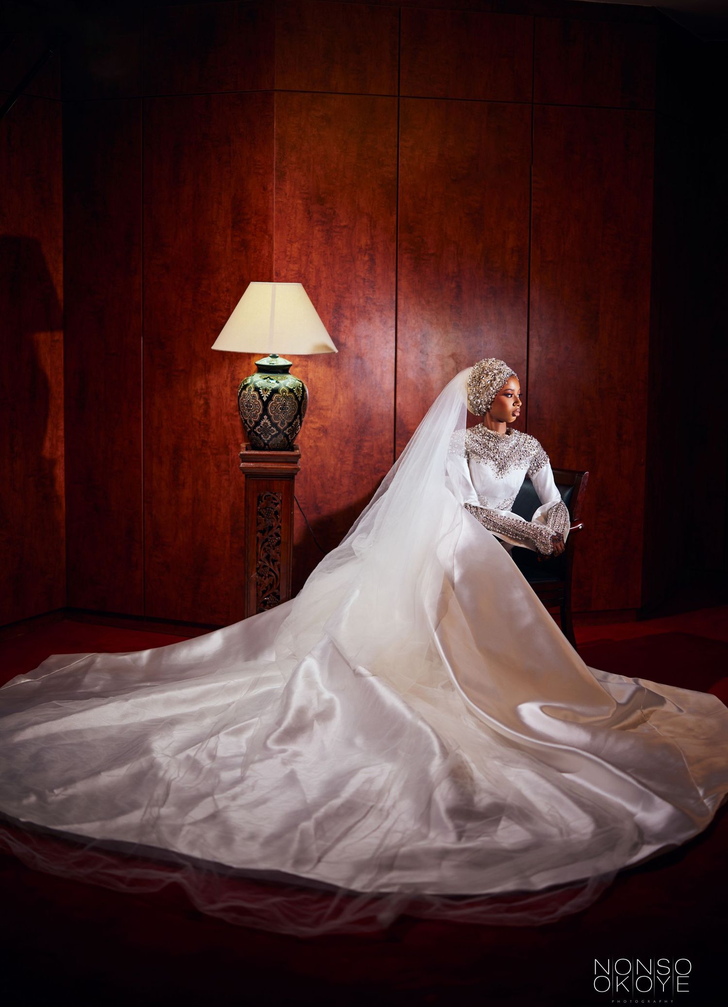 Dramatic bridal portrait showing an elegant white wedding gown with cathedral train against rich wood paneling.