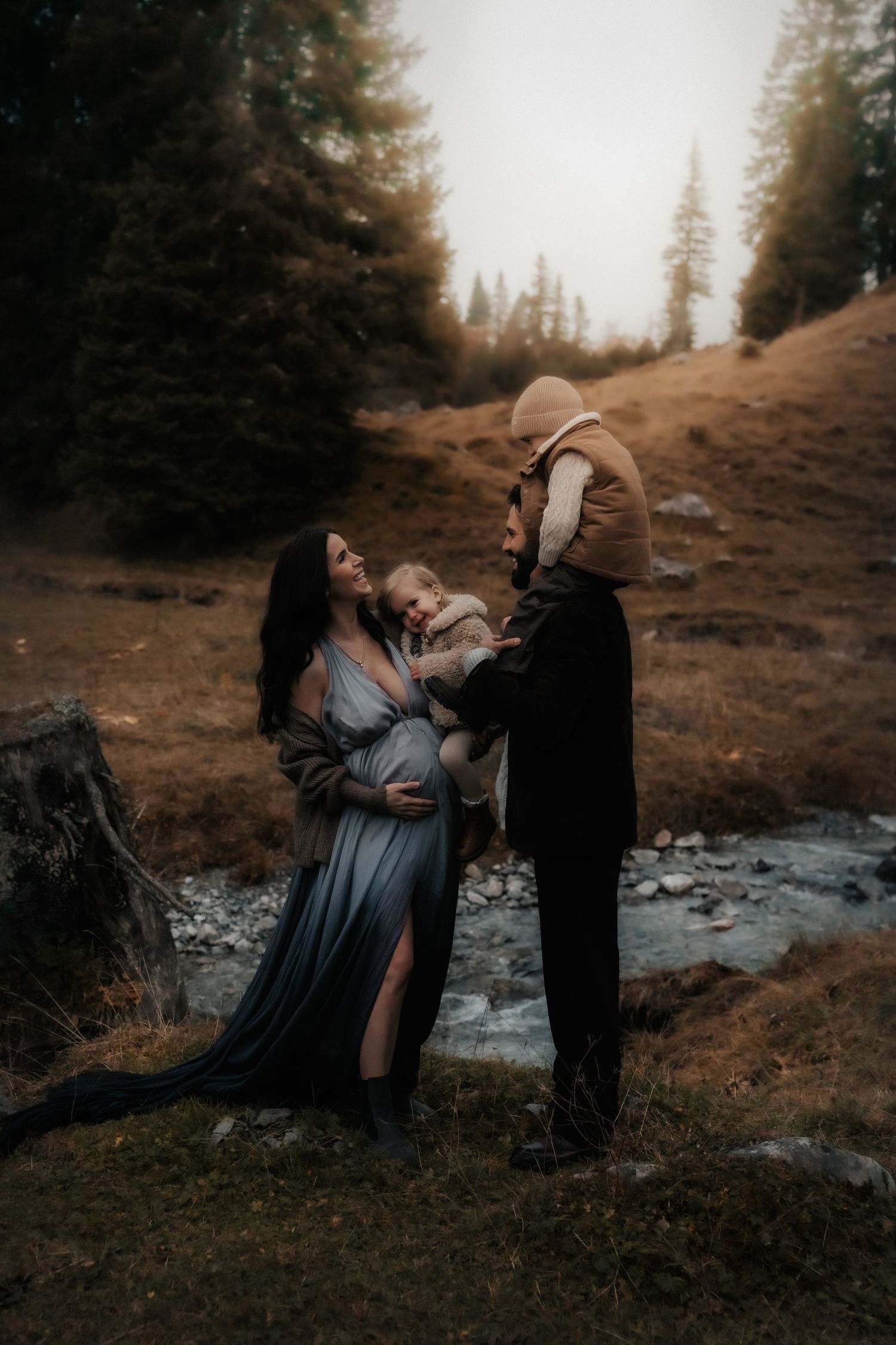 Romantic couple embraces in a dreamy forest setting with evergreen trees and misty atmosphere.
