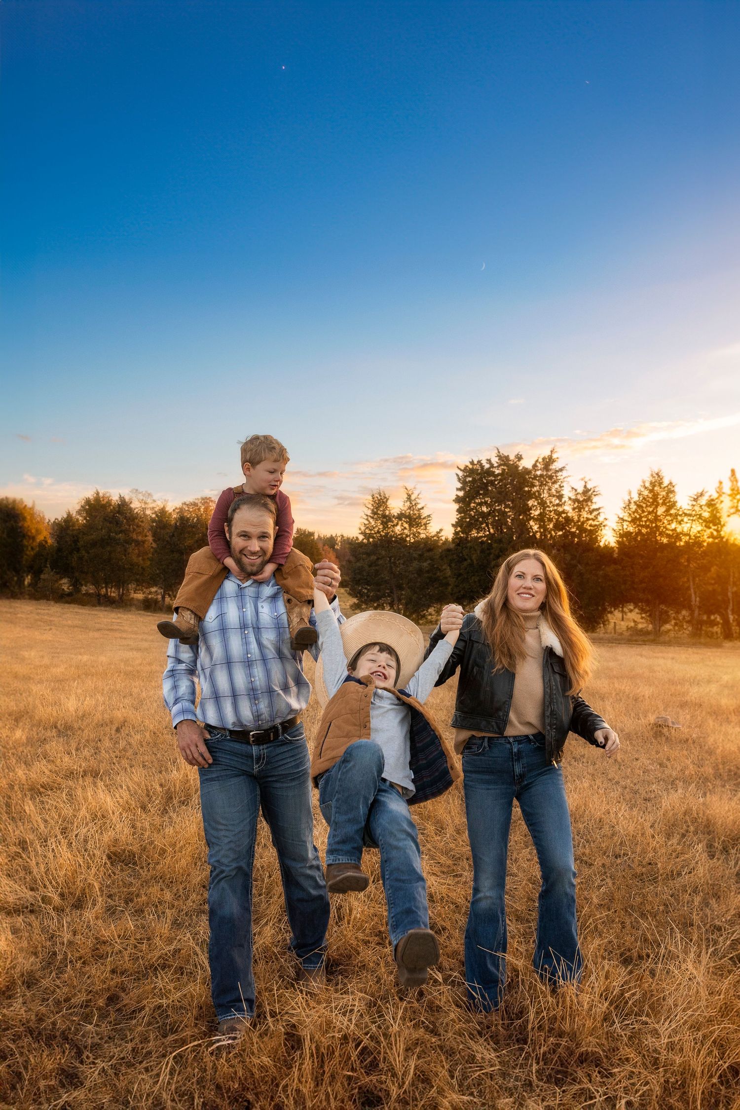 A playful family portrait in a golden field at sunset with children on shoulders.
