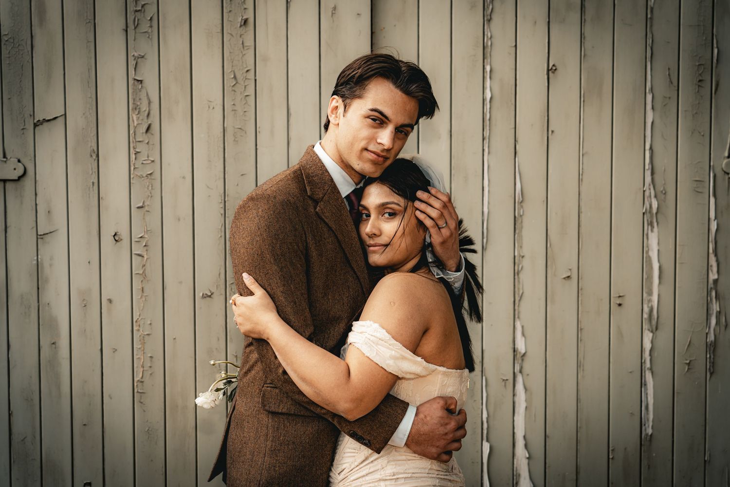 A romantic couple embraces lovingly against a rustic wooden wall background.