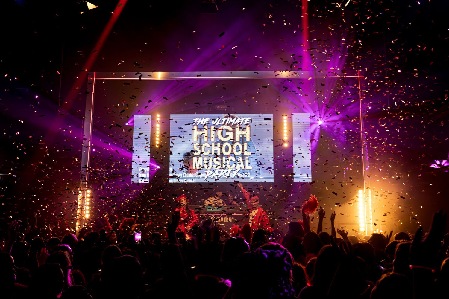 Concert stage lit with purple lighting and High School Musical logo display on screen during live performance.