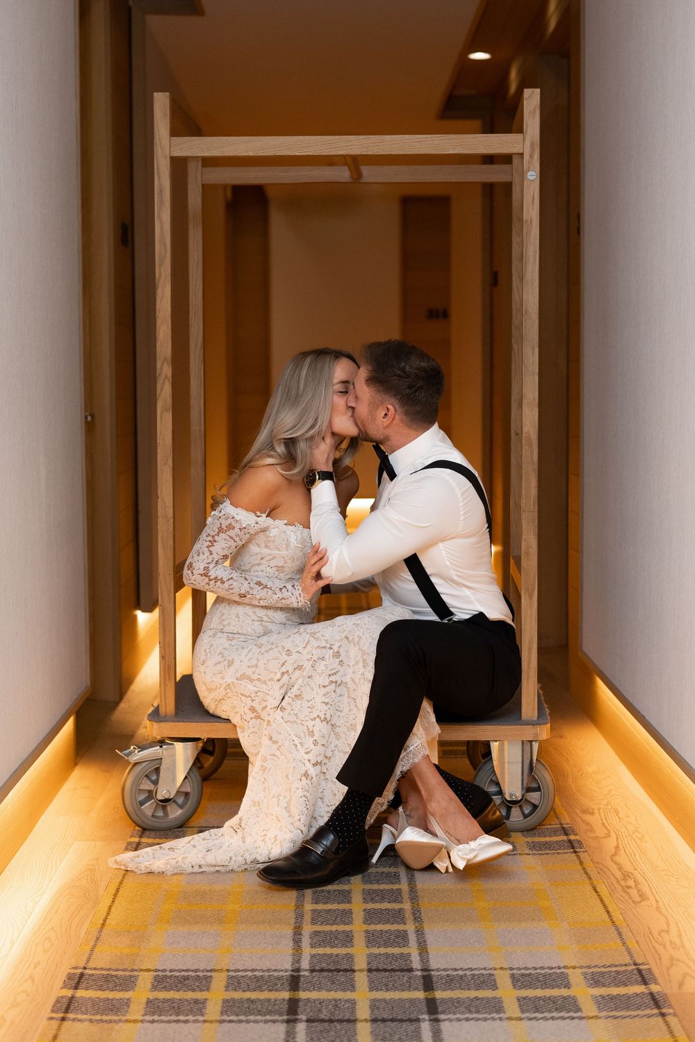Couple in wedding attire sits together on floor of warmly lit hallway with plaid carpet Royal Hotel Picton