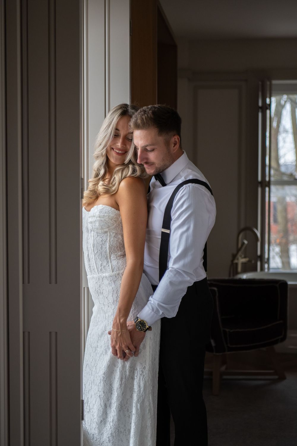 A romantic wedding couple embraces by a window in an intimate indoor setting with moody natural lighting. Royal Hotel Picton