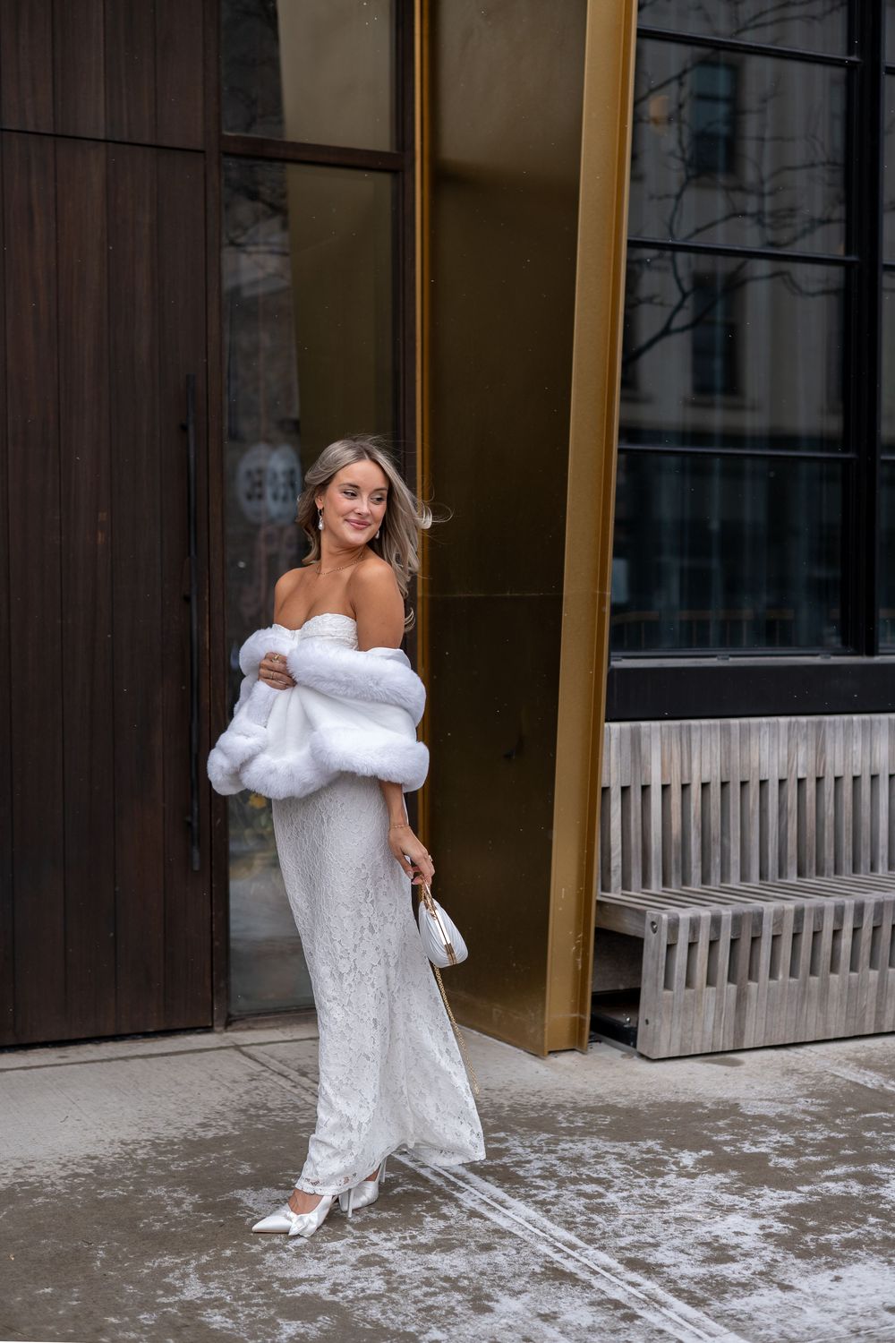 A bride in a white wedding dress and fur wrap stands in front of a building entrance on a snowy winter day. Royal Hotel Picton