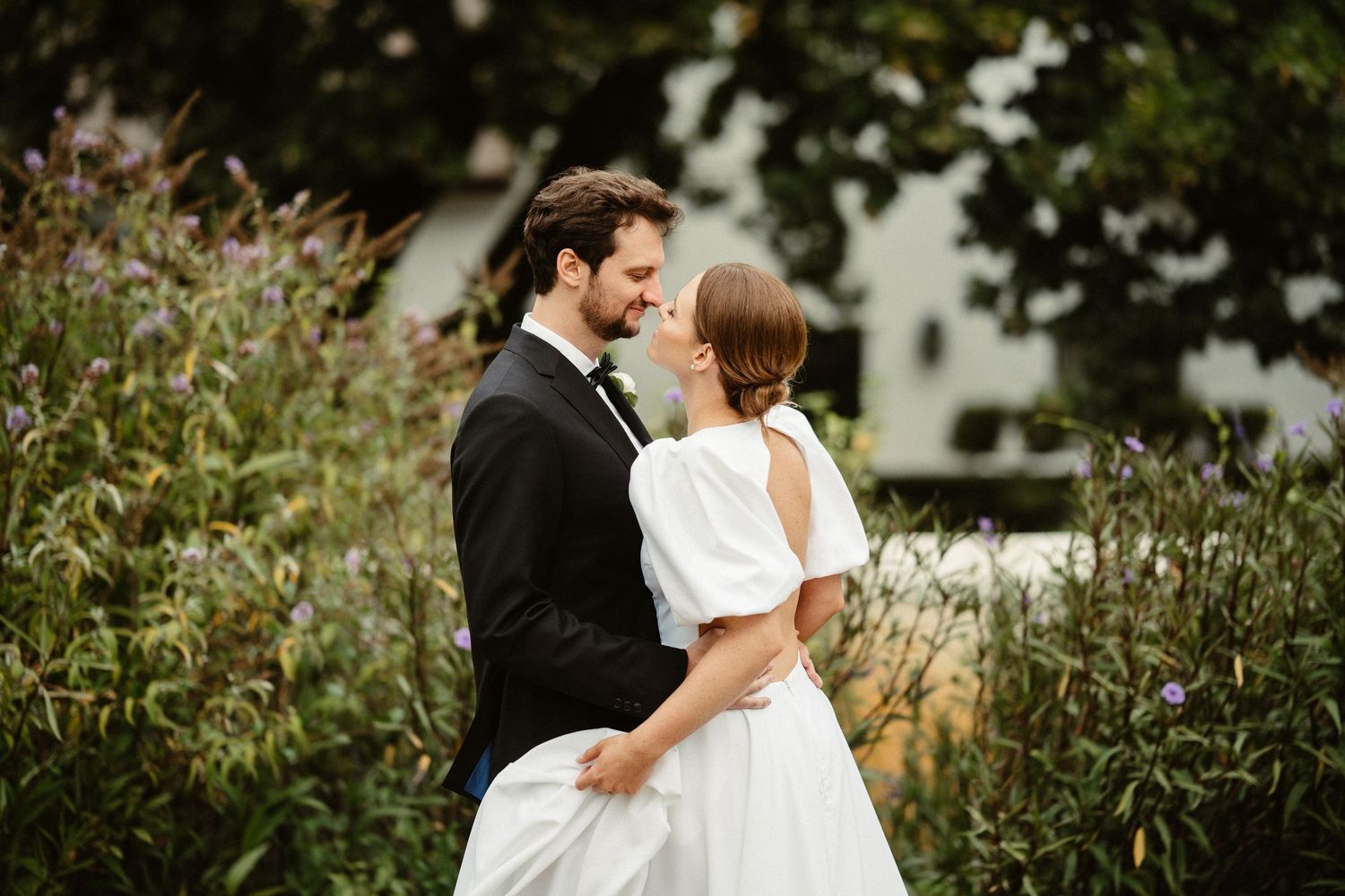 A wedding ceremony takes place outdoors under cloudy skies with white chairs arranged on grass and mountains in background.