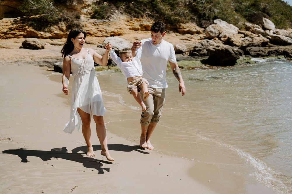 A family walks together along a scenic beach shoreline wearing matching white summer outfits.