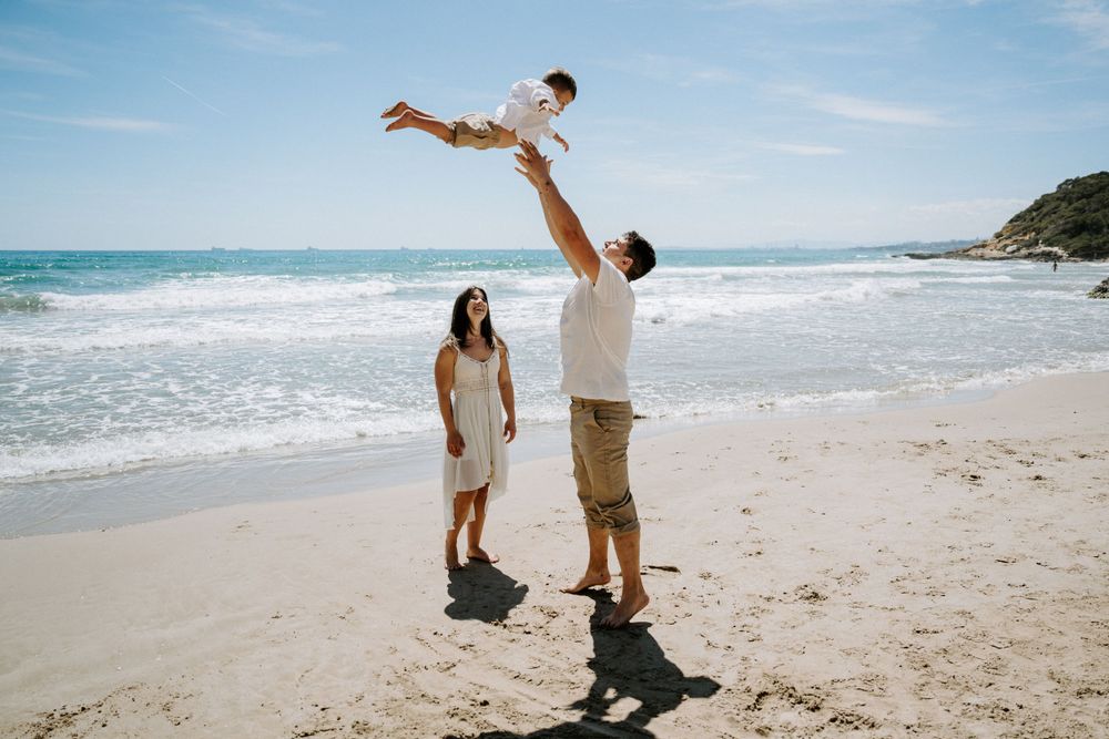 A playful beach scene with a child being lifted high into the air as waves crash behind them.