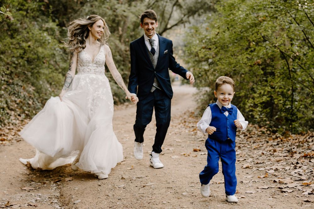 Wedding couple walking through autumn leaves with small child in bright blue outfit.