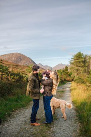 A family and their dog enjoying a walk on a mountain path during golden hour.