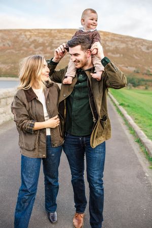 A couple wearing matching brown jackets and jeans walks playfully along a country path.