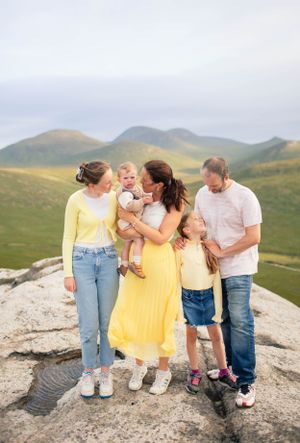 A group gathers on a rocky overlook with scenic mountain views in the background.