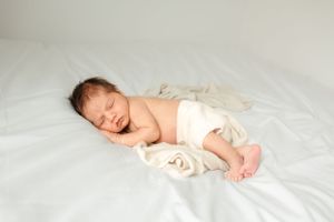Sleeping newborn baby wrapped in soft cream blanket on white bedding.