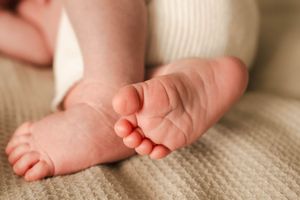 Close-up of tiny newborn baby feet resting on beige knit fabric.