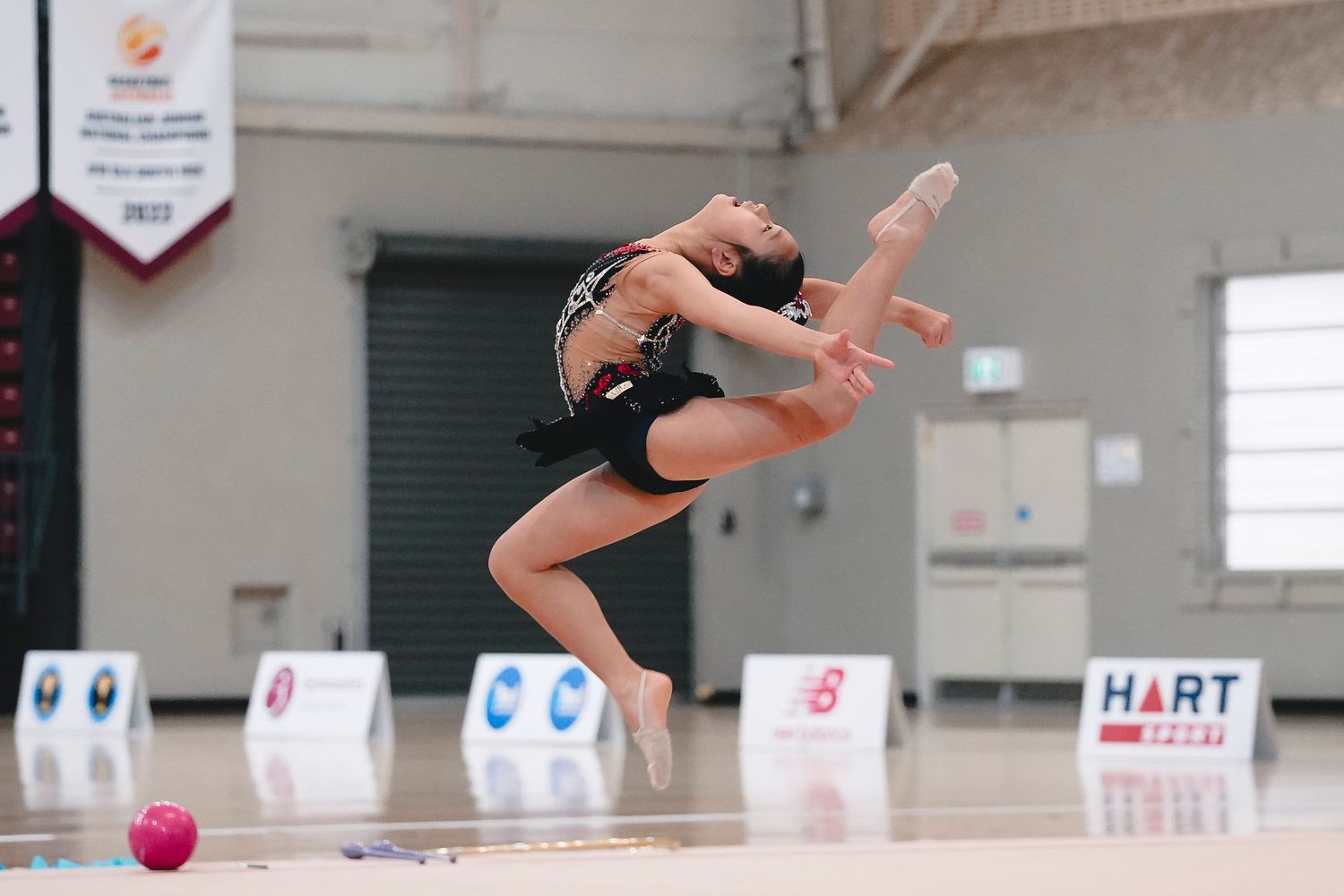Rhythmic gymnast executes powerful leap during floor routine competition.