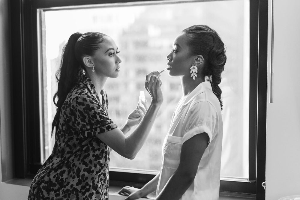 Final wedding preparation moments showing makeup application by window light.