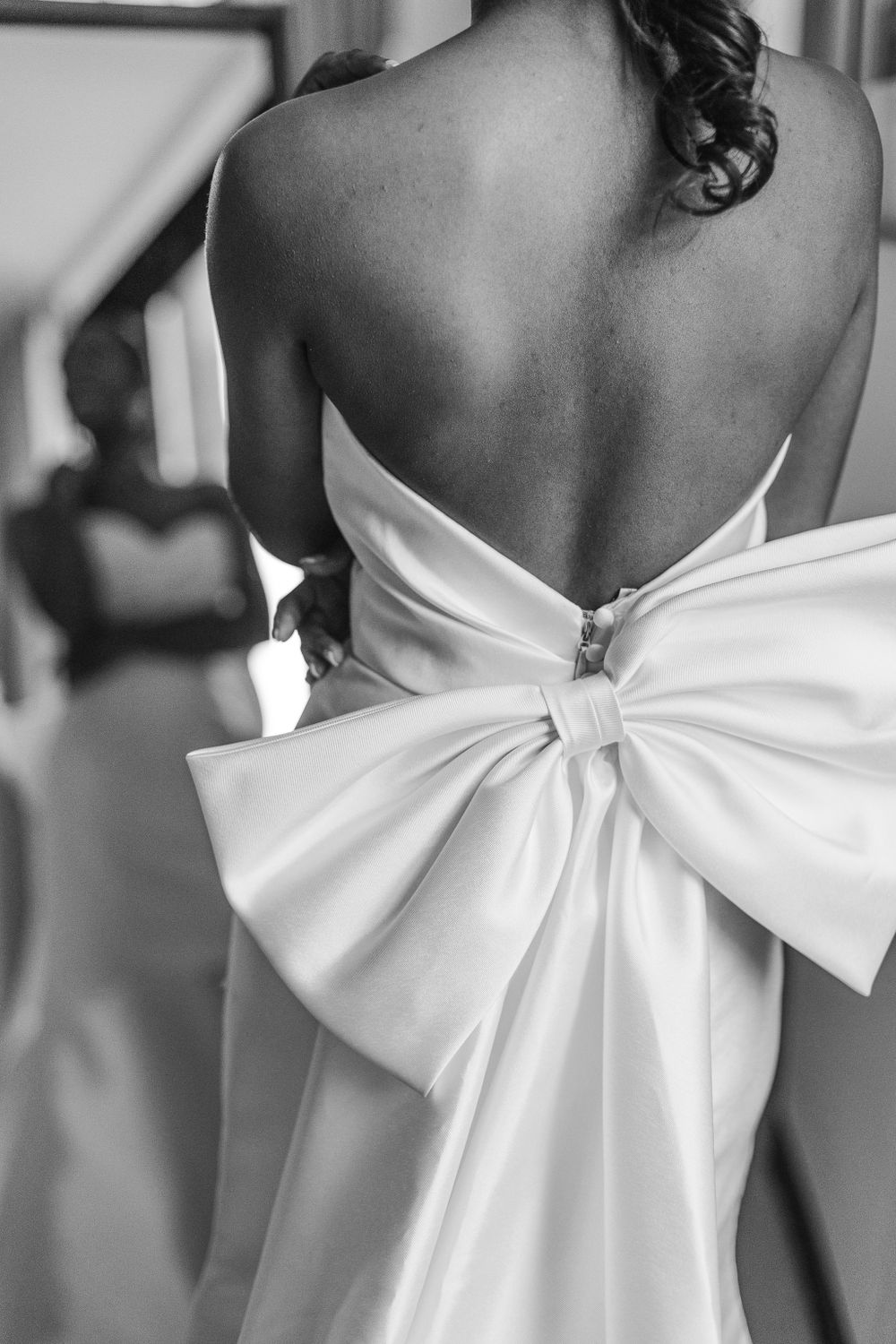 Dramatic black and white photo showcasing back of wedding dress with oversized bow detail.