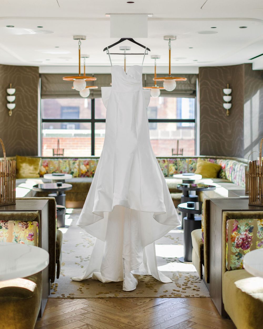 Stunning white wedding dress hanging gracefully in an upscale restaurant setting with natural light.