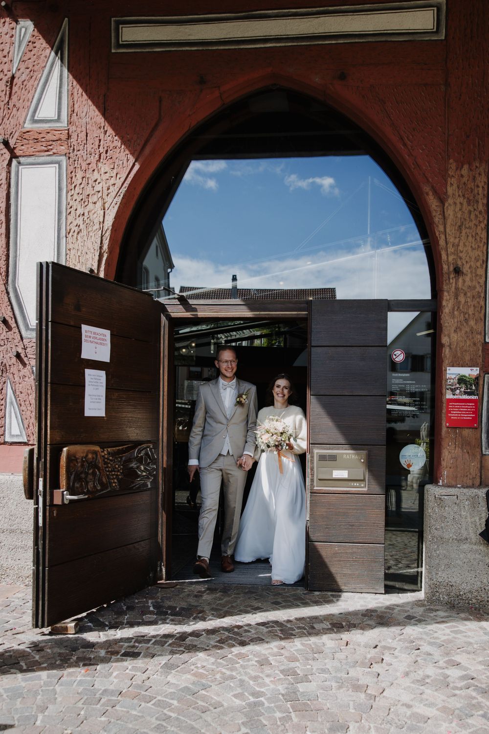 Newlyweds emerging through an arched doorway of historic building.