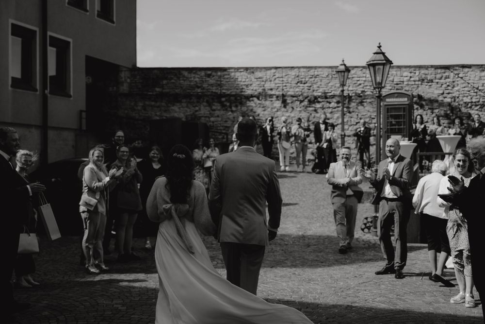 Wedding party and guests mingling in courtyard with stone walls.
