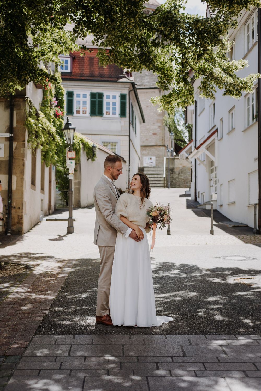 Bride and groom standing together on cobblestone street in European town setting.