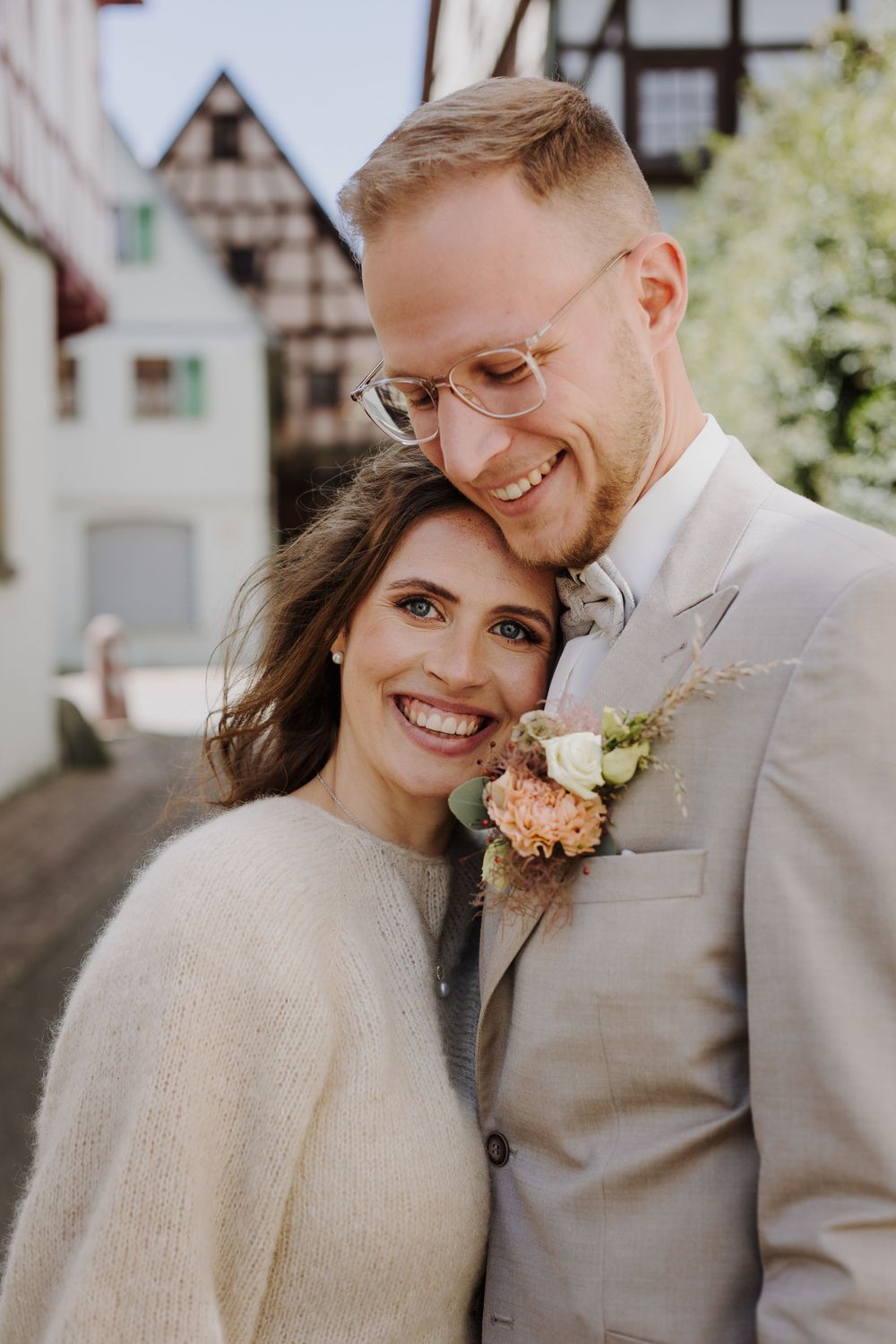 Intimate portrait of couple embracing in soft sunlight against historic architecture.
