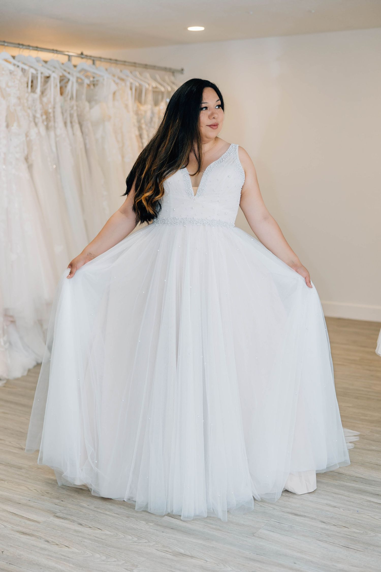 Woman in elegant white V-neck tulle ballgown posing in bridal boutique showroom.