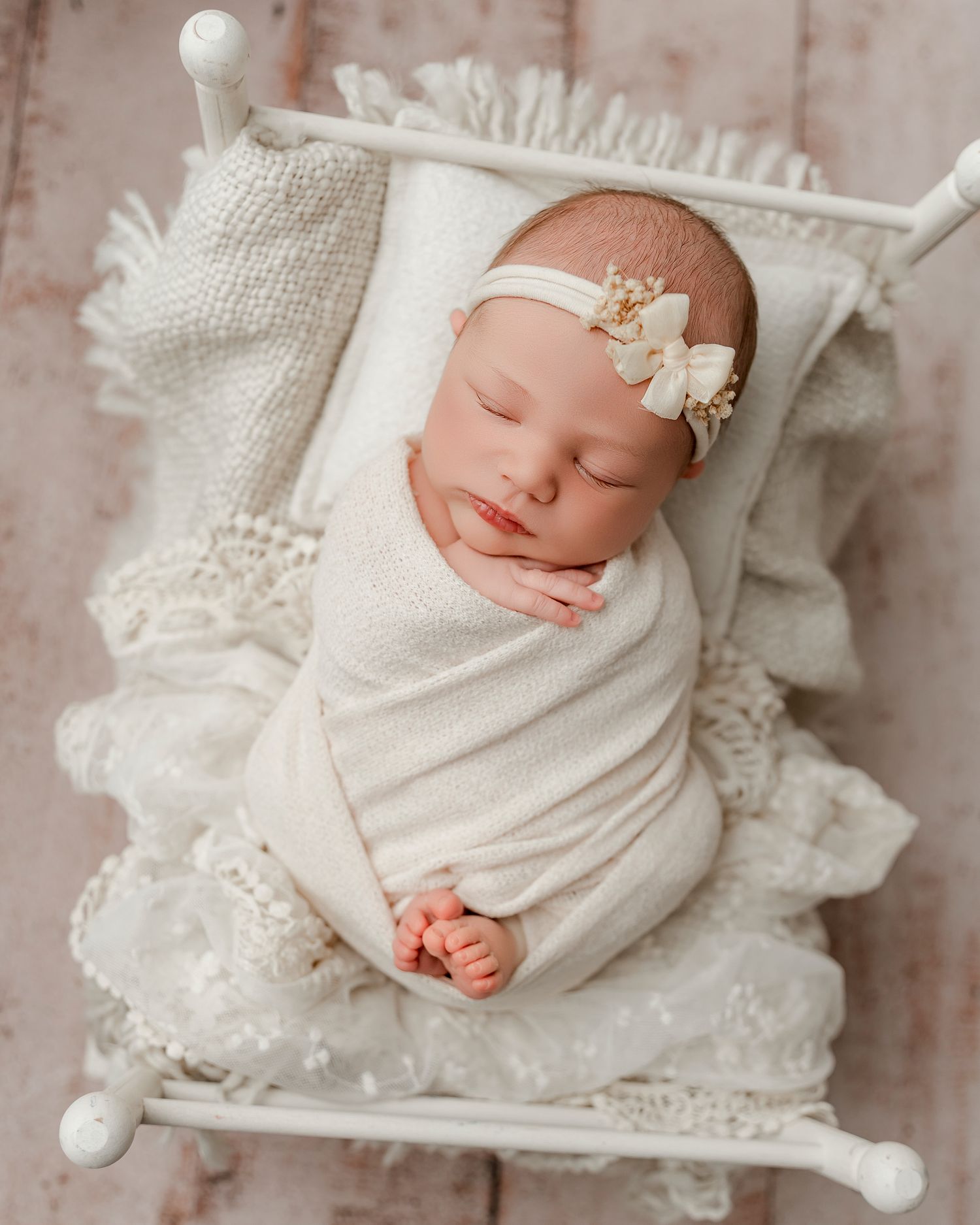 Sleeping newborn wearing white lace outfit and bonnet on pink backdrop.