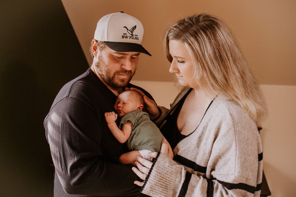 New parents lovingly gazing at their sleeping newborn baby dressed in green.