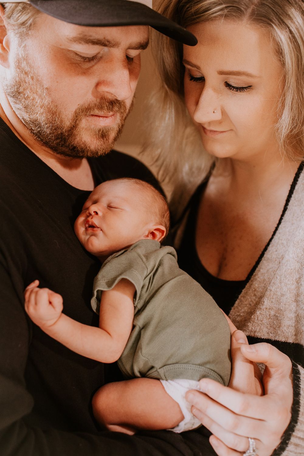 New parents lovingly gaze at their sleeping newborn baby dressed in a green onesie.