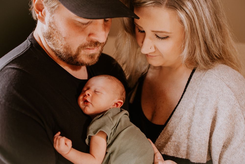 New parents tenderly holding their sleeping newborn baby wrapped in green during a family portrait session.