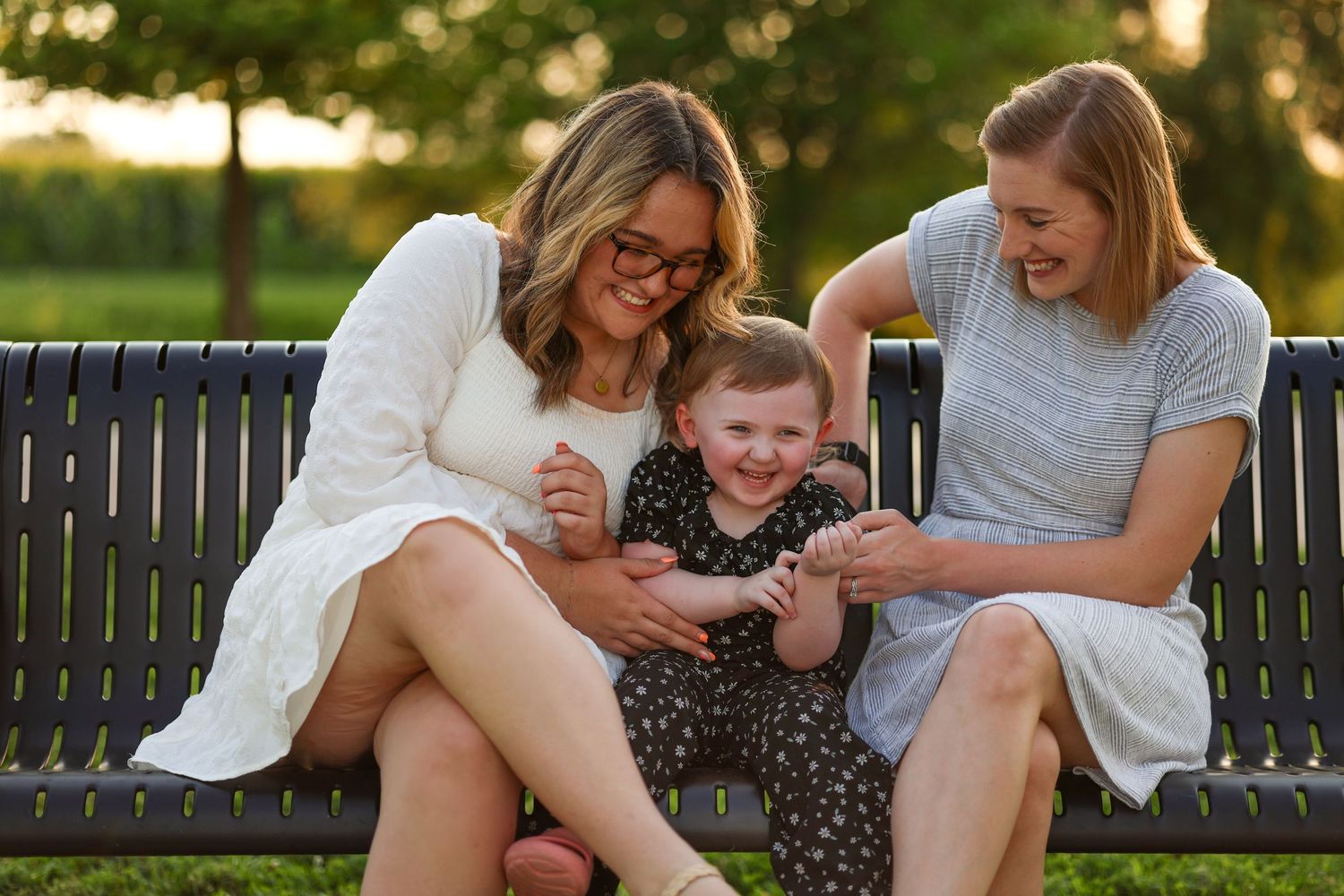 Three people share infectious laughter while relaxing on park bench.