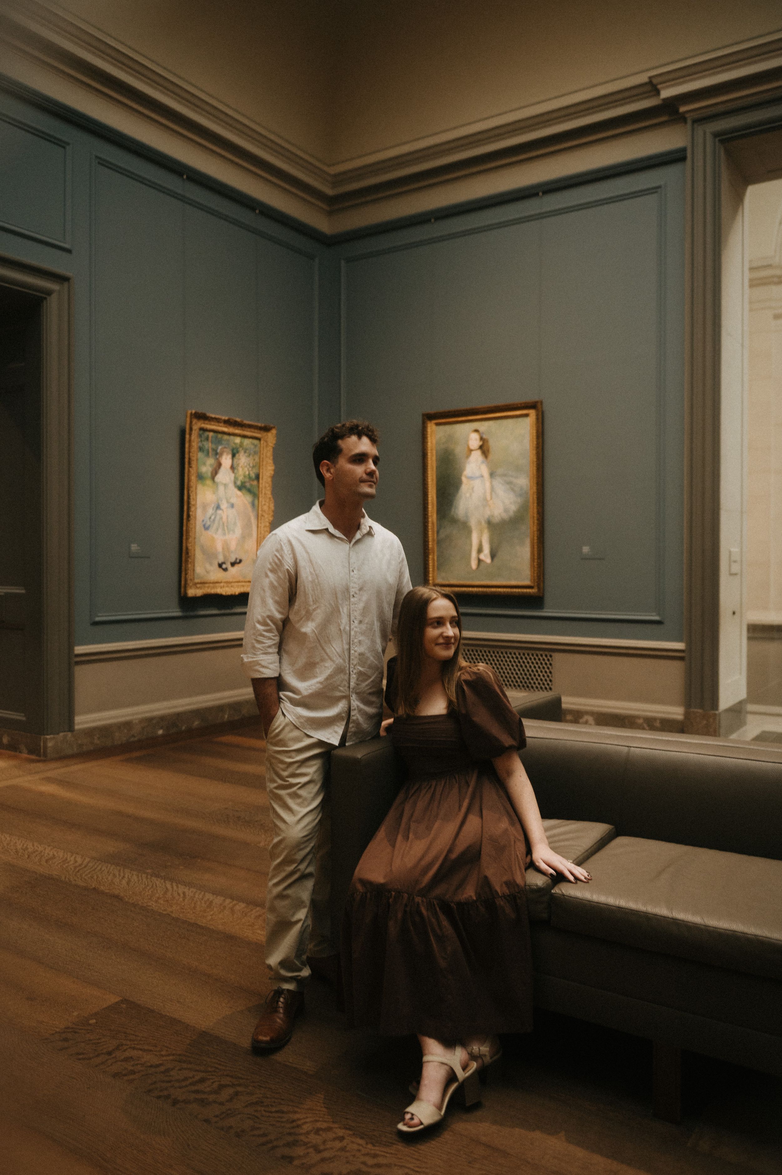 A couple poses artistically in an art gallery with teal walls and hardwood floors.