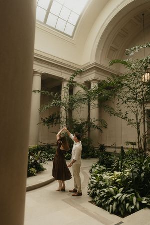 A couple dances gracefully in an elegant indoor atrium filled with lush greenery and natural light.