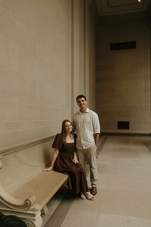 A couple sits together in a minimalist hallway with white walls and tiled floors.