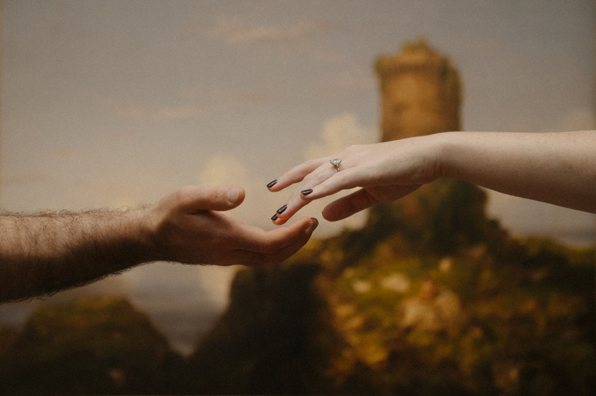 Two hands reach out to each other against a blurred golden background in a tender moment of connection.