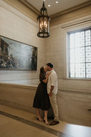 A couple in black and white outfits stand together in an elegant room with hanging lanterns and decorative walls.