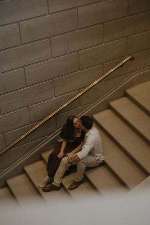 Two people in contrasting outfits lay together on concrete steps in an artistic pose with dramatic lighting.