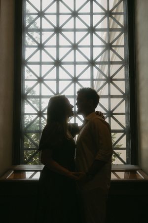 Silhouettes of two people against a geometric window pattern in a museum setting.