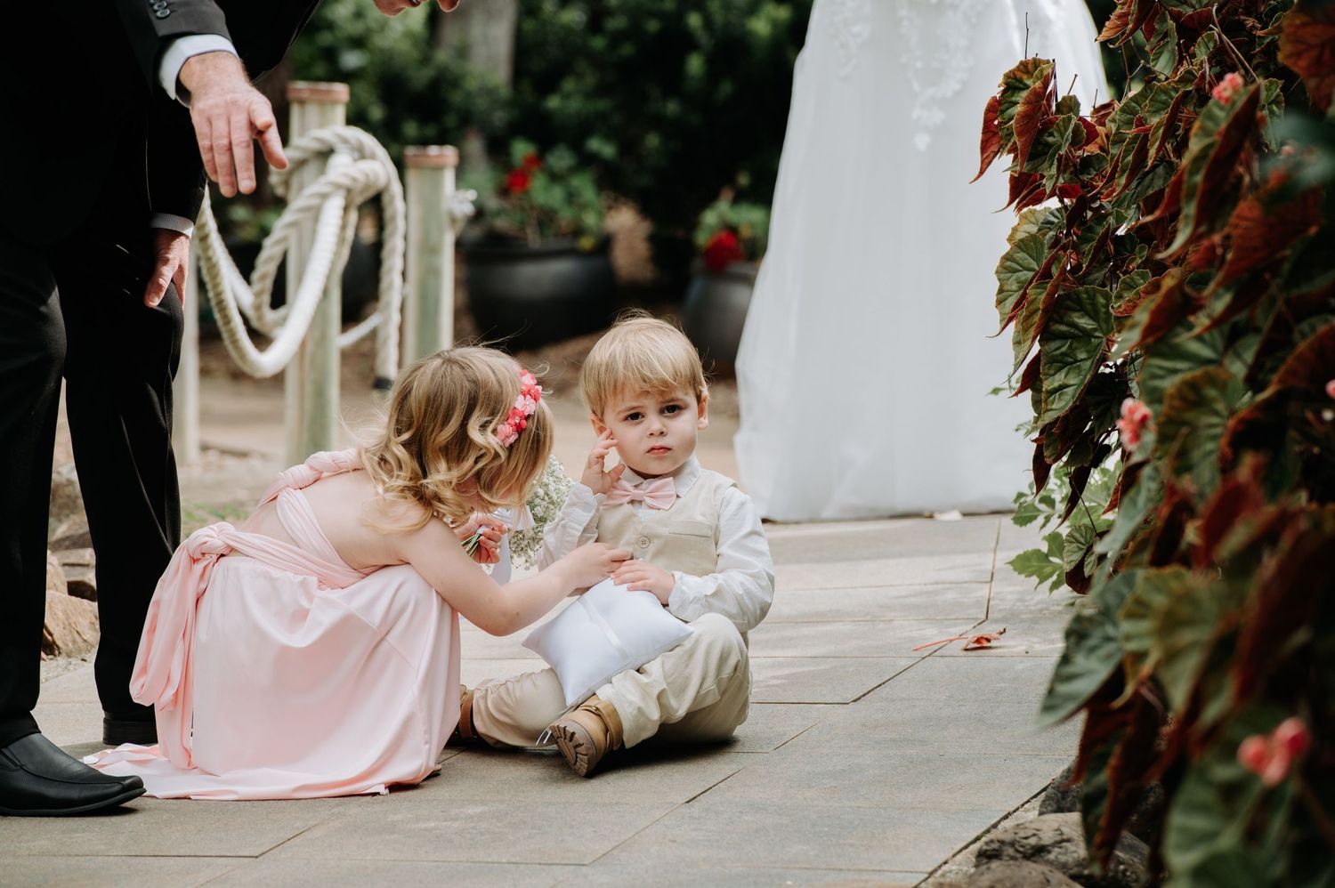 Young children in formal attire sitting together at an outdoor wedding venue.