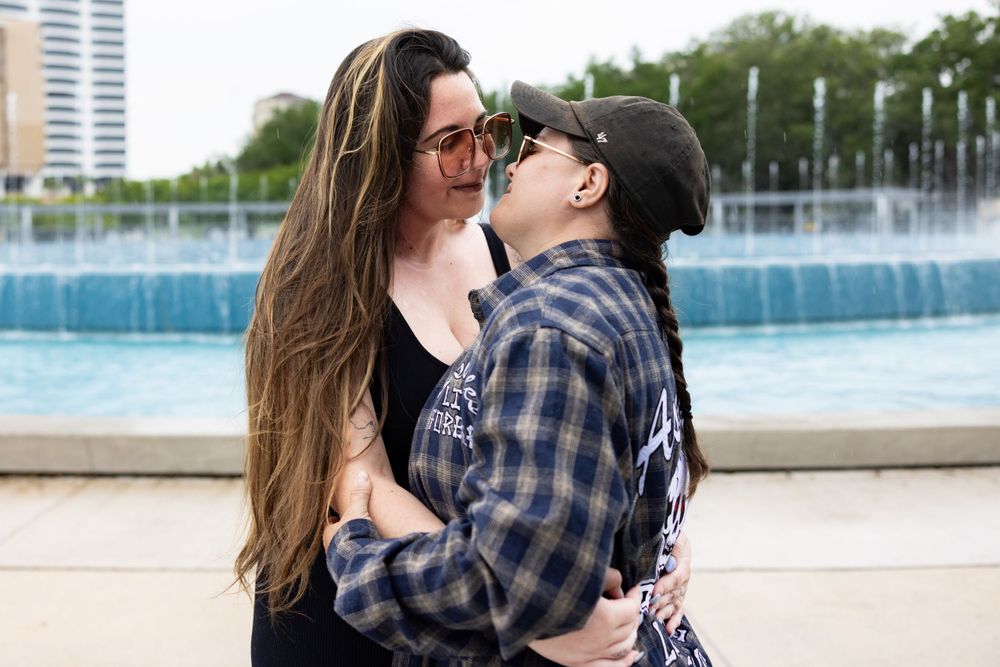 Couple embracing and laughing together near fountain with city backdrop.