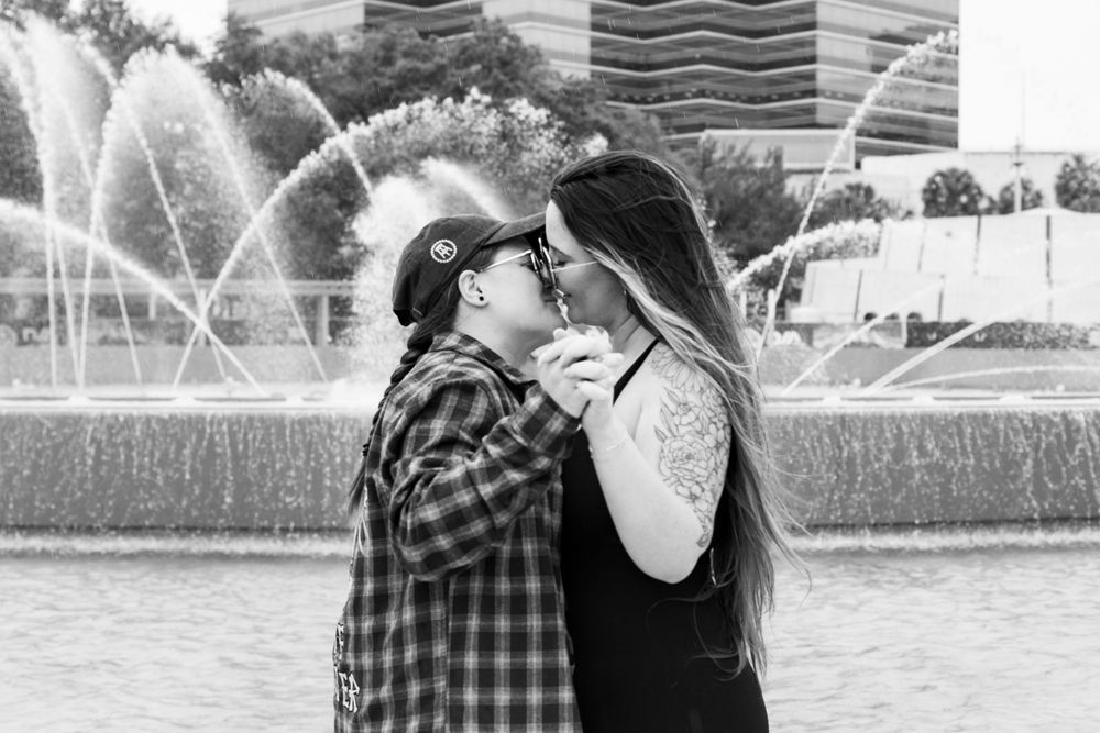 Black and white portrait of couple embracing by fountain.