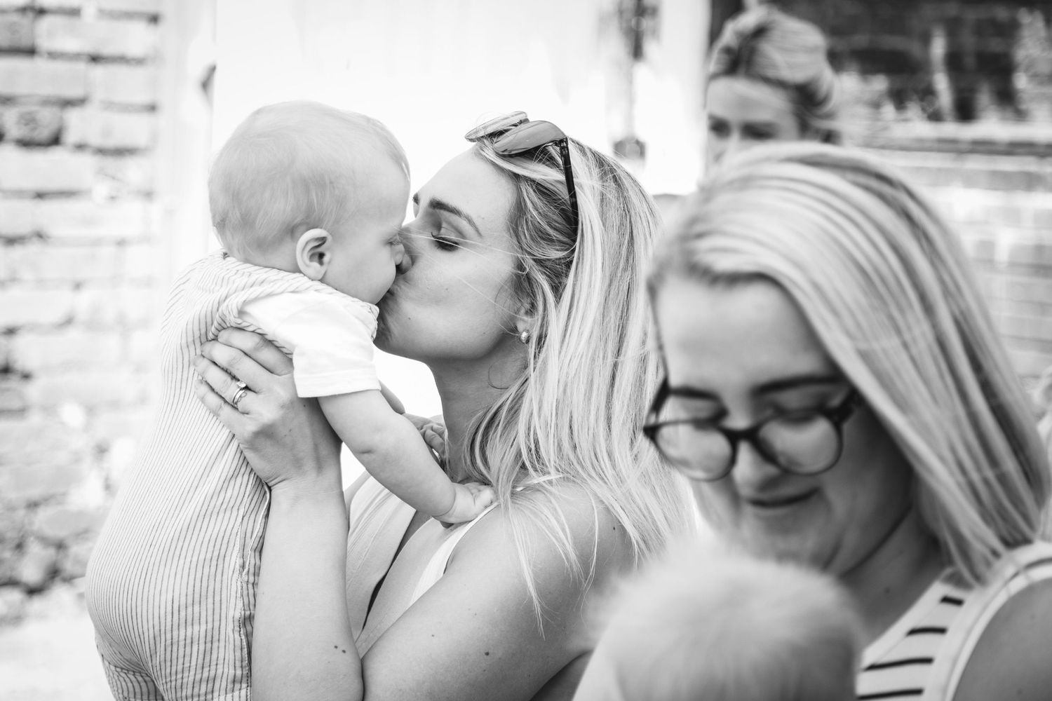 A tender black and white moment showing affection between parent and baby while another looks on with a smile.
