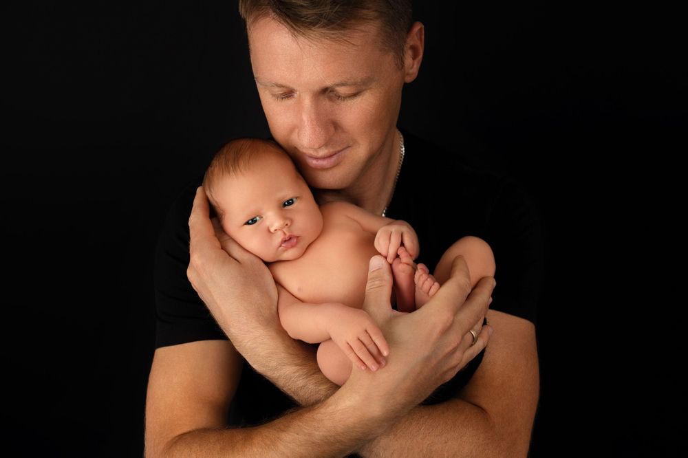 Gentle portrait of parent cradling sleeping newborn against dark background.