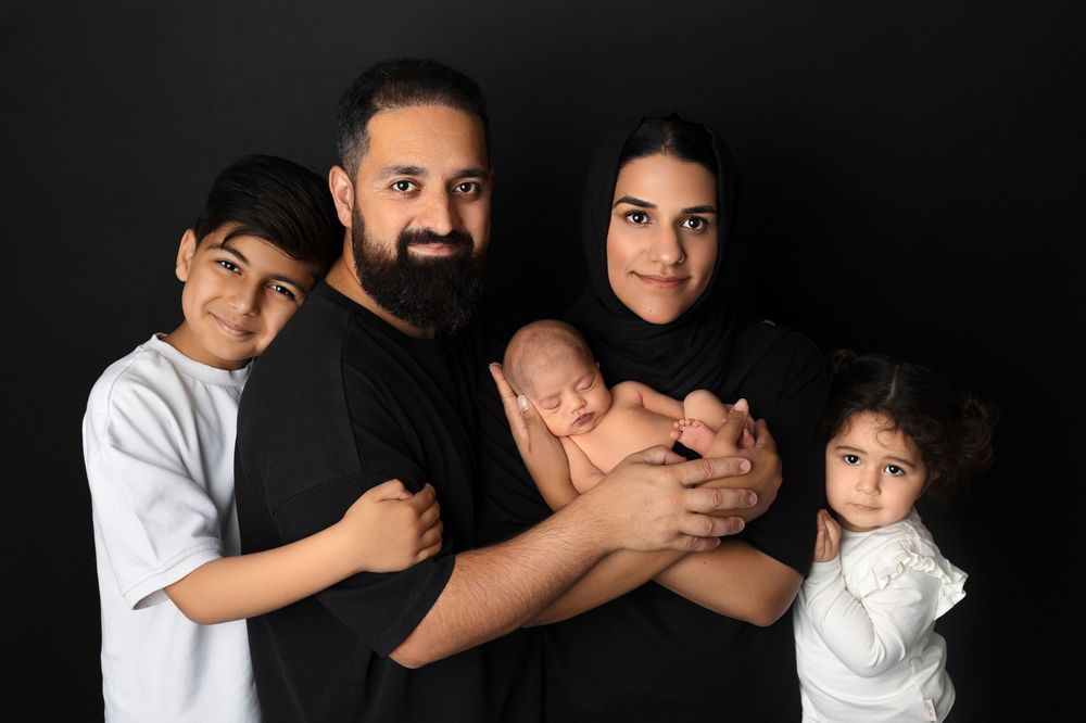 A family of five poses together against a dark background in a studio portrait setting.