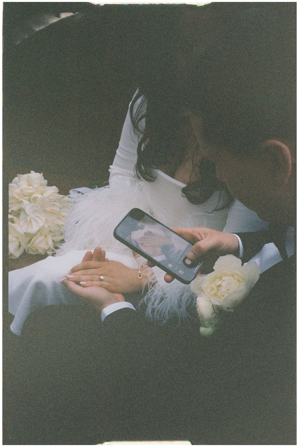 A dreamy vintage-style photo showing hands holding a phone amidst white roses in a moody dark setting.