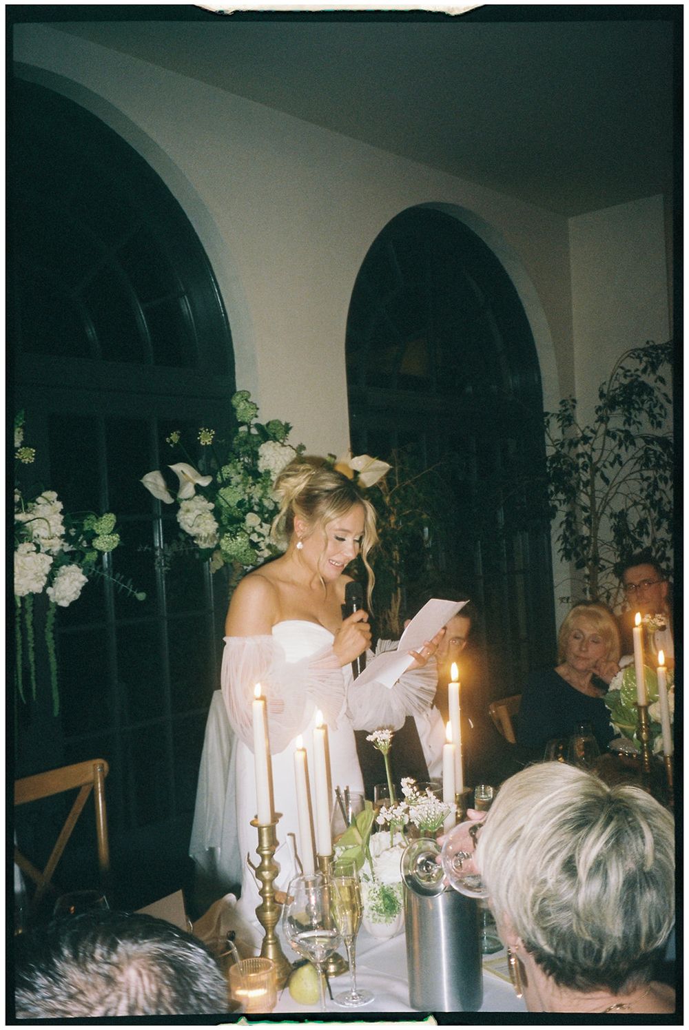 Vintage-style photo of a formal dinner party with candlelight, white flowers and elegant table settings at a luxurious venue.