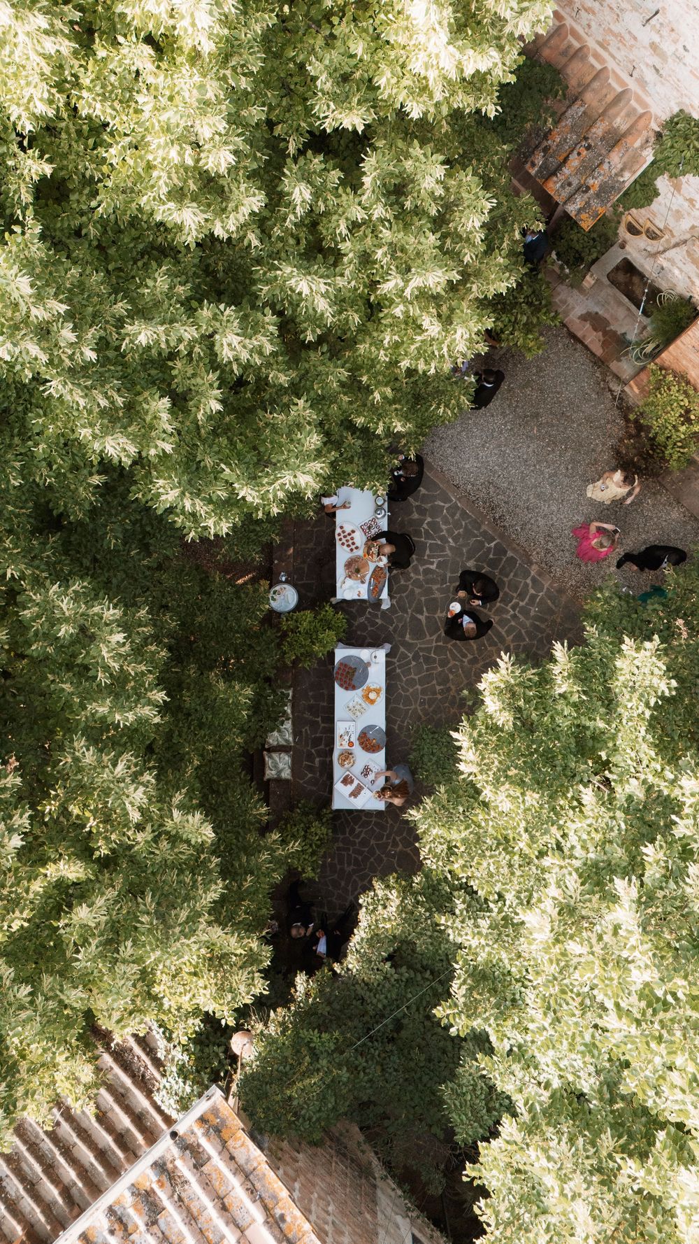 Aerial view of outdoor dining tables surrounded by lush green trees and terracotta roofs.