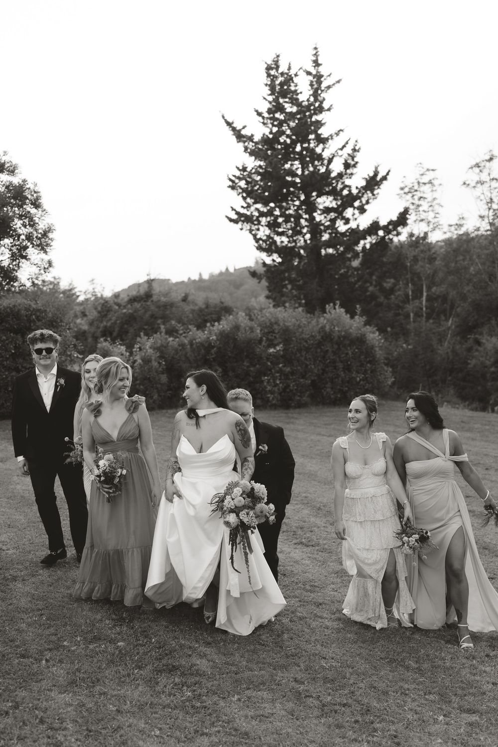 A black and white wedding party walking together outdoors with bridesmaids in flowing dresses and holding bouquets.