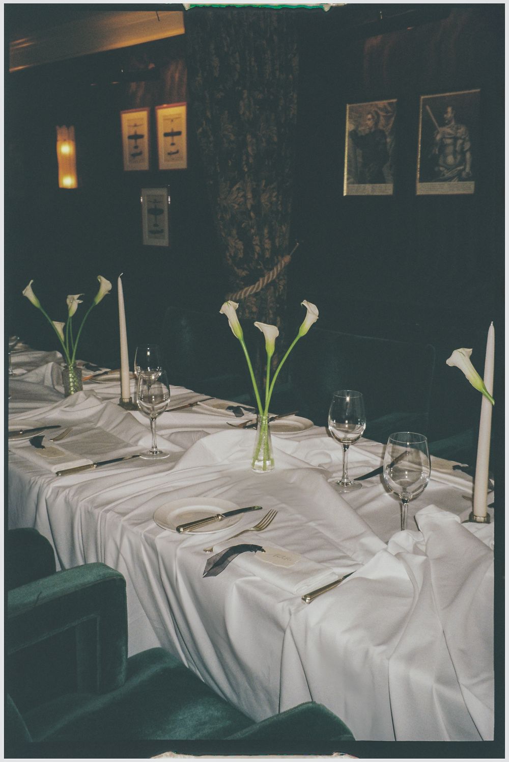 Elegant restaurant table settings with white linens, wine glasses, and simple white calla lily flower arrangements.