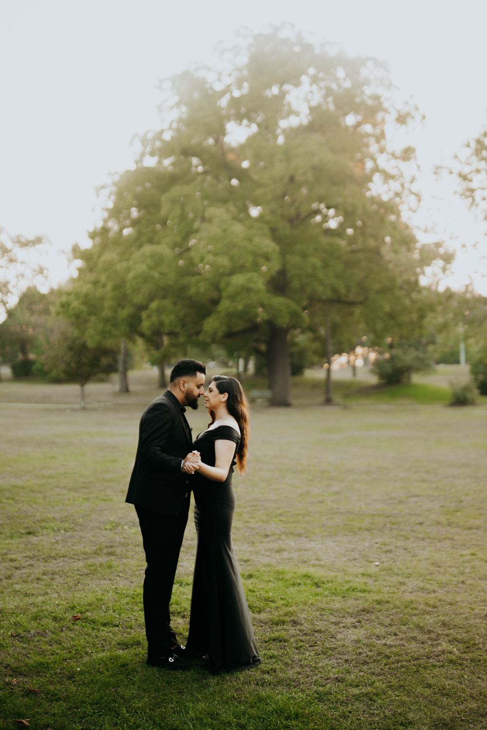 A couple shares an intimate moment in formal wear on a misty lawn with large tree backdrop.